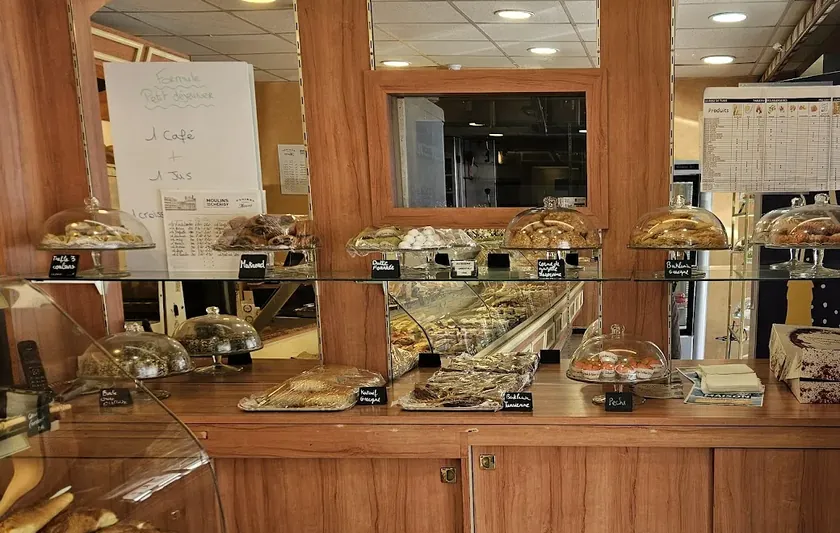Le comptoir en bois de la boutique, avec des cloches en verre posées sur des présentoirs remplis de gâteaux orientaux et leurs ardoises manuscrites.