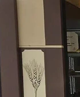 Détail du pilier de la devanture : un panneau crème orné d'un bouquet d'épis de blé dessiné au trait, le même épi que celui du logo.